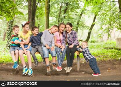 Portrait of beautiful children sitting together on the bench and smiling little boy that push them. Sisyphus metaphor. Kids on the bench