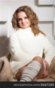 Portrait of beautiful curly woman in white sweater and wool socks sitting on chair