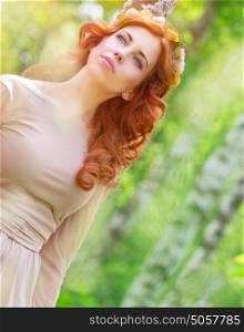 Portrait of beautiful dreamy woman in the park, gentle flower wreath in curly red hair, sensual elegant female enjoying spring nature