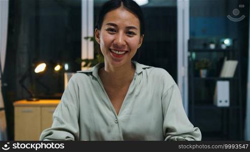 Portrait of beautiful executive businesswoman smart casual wear looking at camera and smiling, happy in modern office workplace night. Young Asia lady talk to colleague in video call meeting at home.