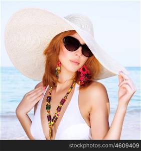 Portrait of beautiful female posing on the beach, wearing stylish big hat and sunglasses, relaxing on luxury beach resort, summer vacation concept