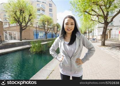 Portrait of beautiful fit woman standing by canal against buildings