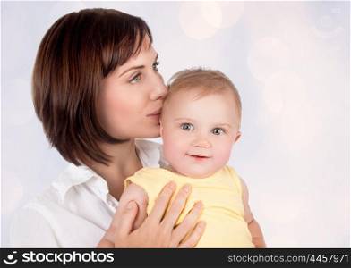 Portrait of beautiful gentle mother kissing her precious little baby over blur background, young loving family, enjoying motherhood