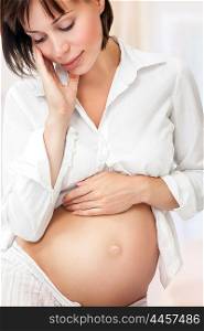 Portrait of beautiful gentle pregnant woman at home, with tenderness looking on her tummy, new life, happy healthy pregnancy