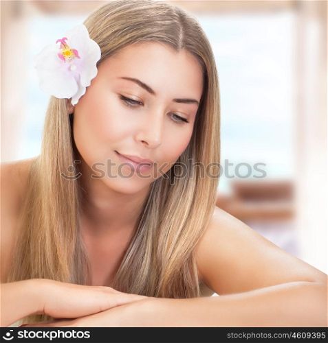 Portrait of beautiful gentle woman with orchid flower in hair in spa salon, enjoying alternative treatment, natural beauty concept
