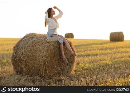 Portrait of beautiful girl on haystack roll on harvested wheat field in the summer. Selective focus. Portrait of beautiful girl on haystack roll on harvested wheat field in the summer. Selective focus.