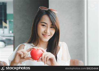 Portrait of beautiful happy Asian woman smiling and holding a red heart. Concept of love and relationship.