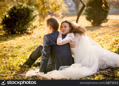 Portrait of beautiful happy bride hugging groom sitting on yellow leaves at park