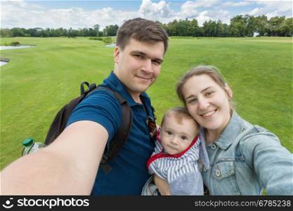 Portrait of beautiful happy family with baby boy making selfie at park