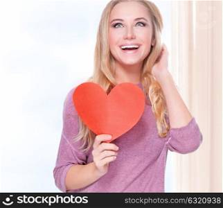 Portrait of beautiful happy girl holding in hands red heart shaped greeting card, celebrating holiday at home, Valentine day concept