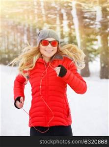 Portrait of beautiful happy runner outdoors, cute blond female running in the winter park and listening music in headphones, active and healthy lifestyle