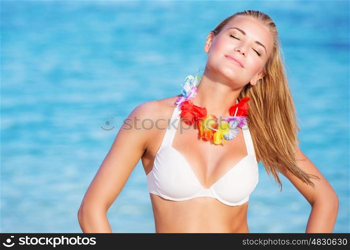 Portrait of beautiful happy woman on the beach, enjoying bright sunny day with closed eyes, wearing traditional Hawaiian necklace of flowers, active summer vacation