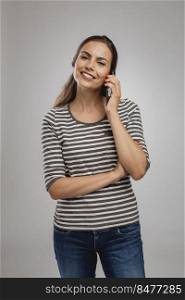 Portrait of beautiful happy young woman over a gray background talking at phone 