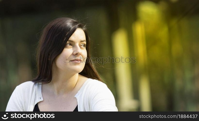 Portrait of beautiful Hispanic young woman with long hair looking to the right against a background of unfocused trees during sunset with copy space. Portrait of beautiful Hispanic young woman with long hair looking to the right against a background of unfocused trees during sunset