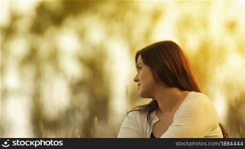 Portrait of beautiful Hispanic young woman with long hair looking to the right against a background of unfocused trees during sunset with copy space. Portrait of beautiful Hispanic young woman with long hair looking to the right against a background of unfocused trees during sunset