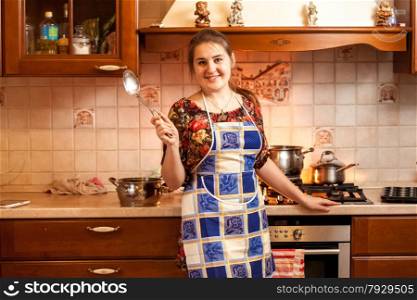 Portrait of beautiful housewife holding soup ladle on kitchen