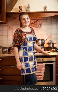 Portrait of beautiful housewife posing against gas stove with saucepans