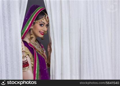 Portrait of beautiful Indian bride smiling amidst curtains