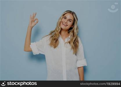Portrait of beautiful joyful blonde woman making on camera ok gesture or okay sign with fingers, female smiling happily and showing perfect white teeth. Body language concept. Portrait of beautiful joyful blonde girl making on camera ok gesture with fingers