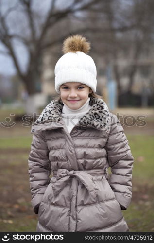 Portrait of beautiful little girl in a white knitted hat autumn