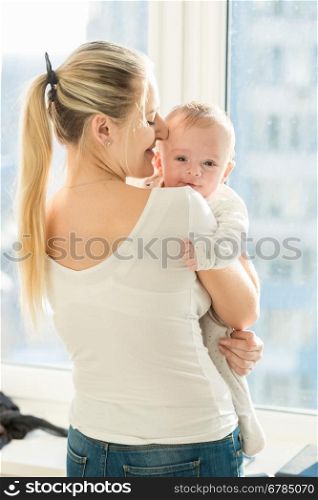 Portrait of beautiful mother embracing her 3 months old baby boy at window