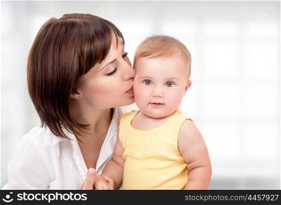 Portrait of beautiful mother with pleasure kissing her cute adorable little daughter at home, happy young family, love and happiness concept