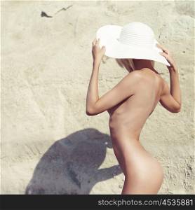 Portrait of beautiful nude woman with white hat. Naked lady on the beach