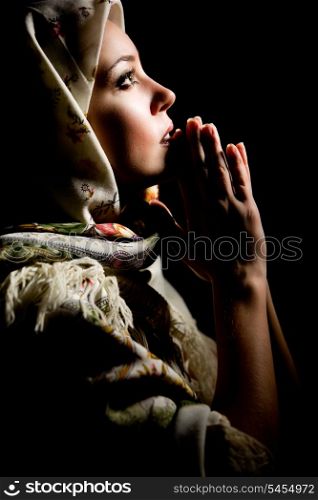 Portrait of beautiful praying girl with old russian shawl on head on black background. Retouched&#xA;