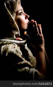 Portrait of beautiful praying girl with old russian shawl on head on black background. Retouched&#xA;