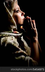 Portrait of beautiful praying girl with old russian shawl on head on black background. &#xA;