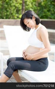 Portrait of beautiful pregnant asian young woman relax in the park, girl with belly sitting at swimming pool for wellness, tummy girl, health care concept.