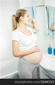 Portrait of beautiful pregnant woman brushing teeth at bathroom