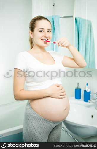 Portrait of beautiful pregnant woman brushing teeth in bathroom at morning