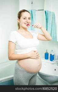 Portrait of beautiful pregnant woman brushing teeth in bathroom at morning