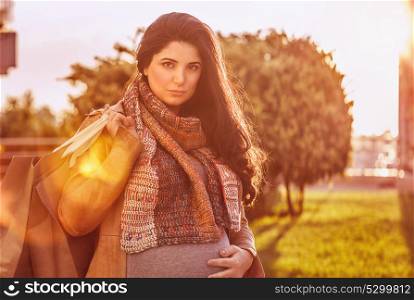 Portrait of beautiful pregnant woman with shopping bag outdoors in sunny day, happy shopping in pregnancy period