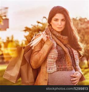 Portrait of beautiful pregnant woman with shopping bag outdoors in sunny day, happy shopping in pregnancy period