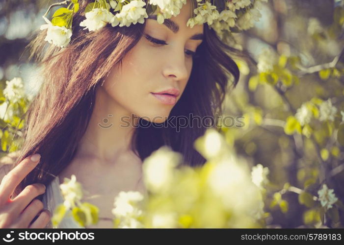 Portrait of beautiful romantic lady in a wreath of apple trees in the summer garden