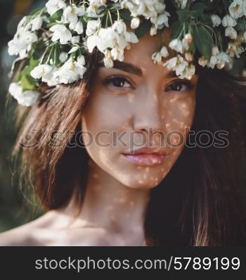 Portrait of beautiful romantic lady in a wreath of apple trees in the summer garden