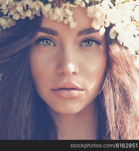 Portrait of beautiful romantic lady in a wreath of apple trees in the summer garden