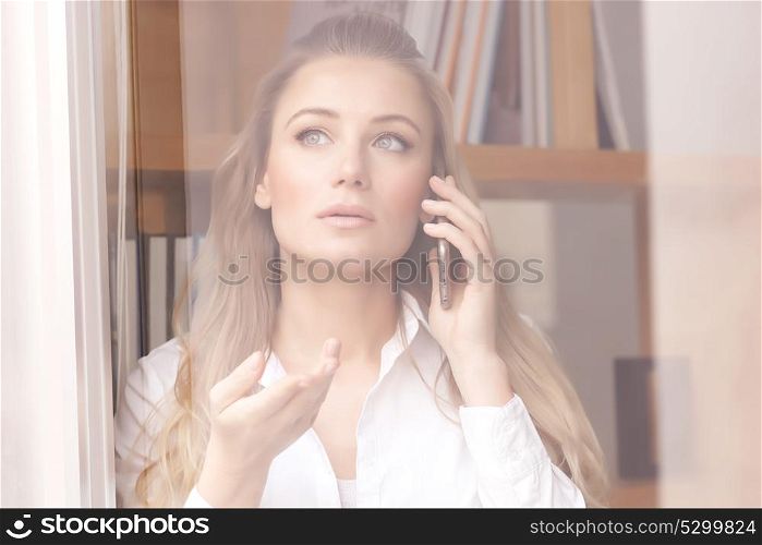 Portrait of beautiful serious business woman speaking on the phone and looking through the window, explaining something to business partner