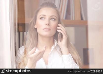 Portrait of beautiful serious business woman speaking on the phone and looking through the window, explaining something to business partner
