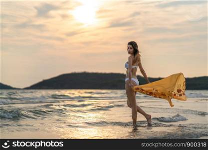 Portrait of beautiful sexy Asian girl in bikini, posing on the beach at sunset. Model photo shoot, sea travel, or holiday vacation concept