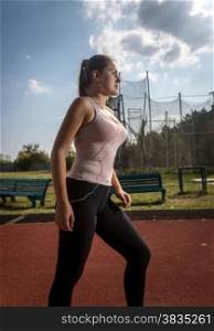 Portrait of beautiful slim woman jogging on sport arena at hot sunny day