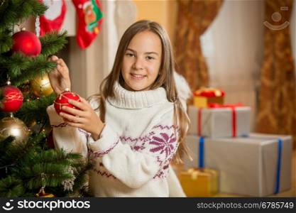 Portrait of beautiful smiling girl decorating Christmas tree with baubles