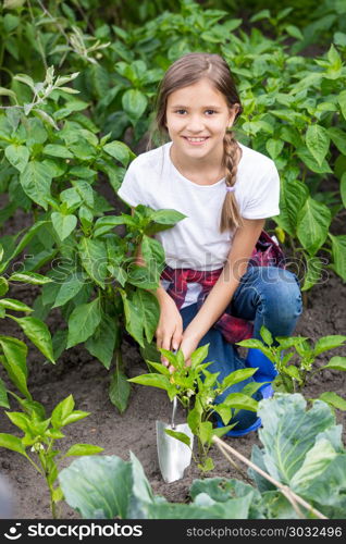 Portrait of beautiful smiling girl spudding garden bed with growing vegetables with trowel. Beautiful smiling girl spudding garden bed with growing vegetables with trowel