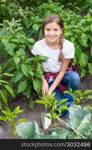Portrait of beautiful smiling girl spudding garden bed with growing vegetables with trowel. Beautiful smiling girl spudding garden bed with growing vegetables with trowel