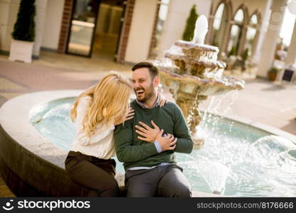 Portrait of beautiful smiling love couple sitting by fountain on a sunny day