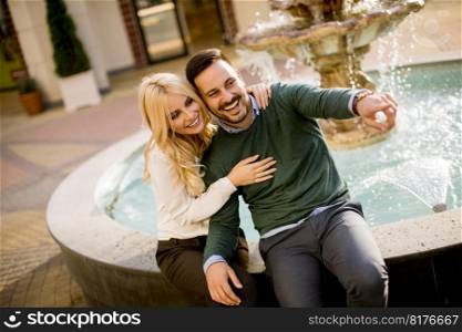 Portrait of beautiful smiling love couple sitting by fountain on a sunny day