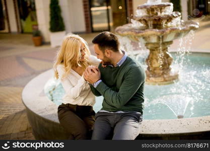 Portrait of beautiful smiling love couple sitting by fountain on a sunny day