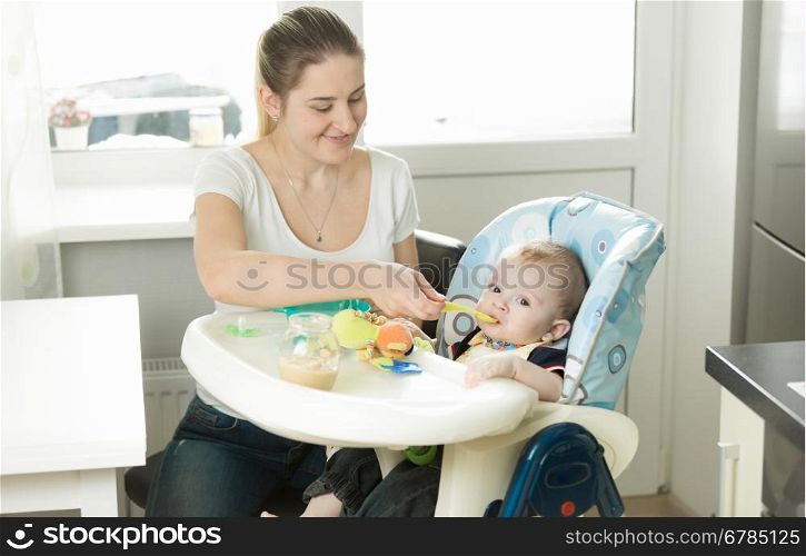 Portrait of beautiful smiling mother feeding her baby on kitchen